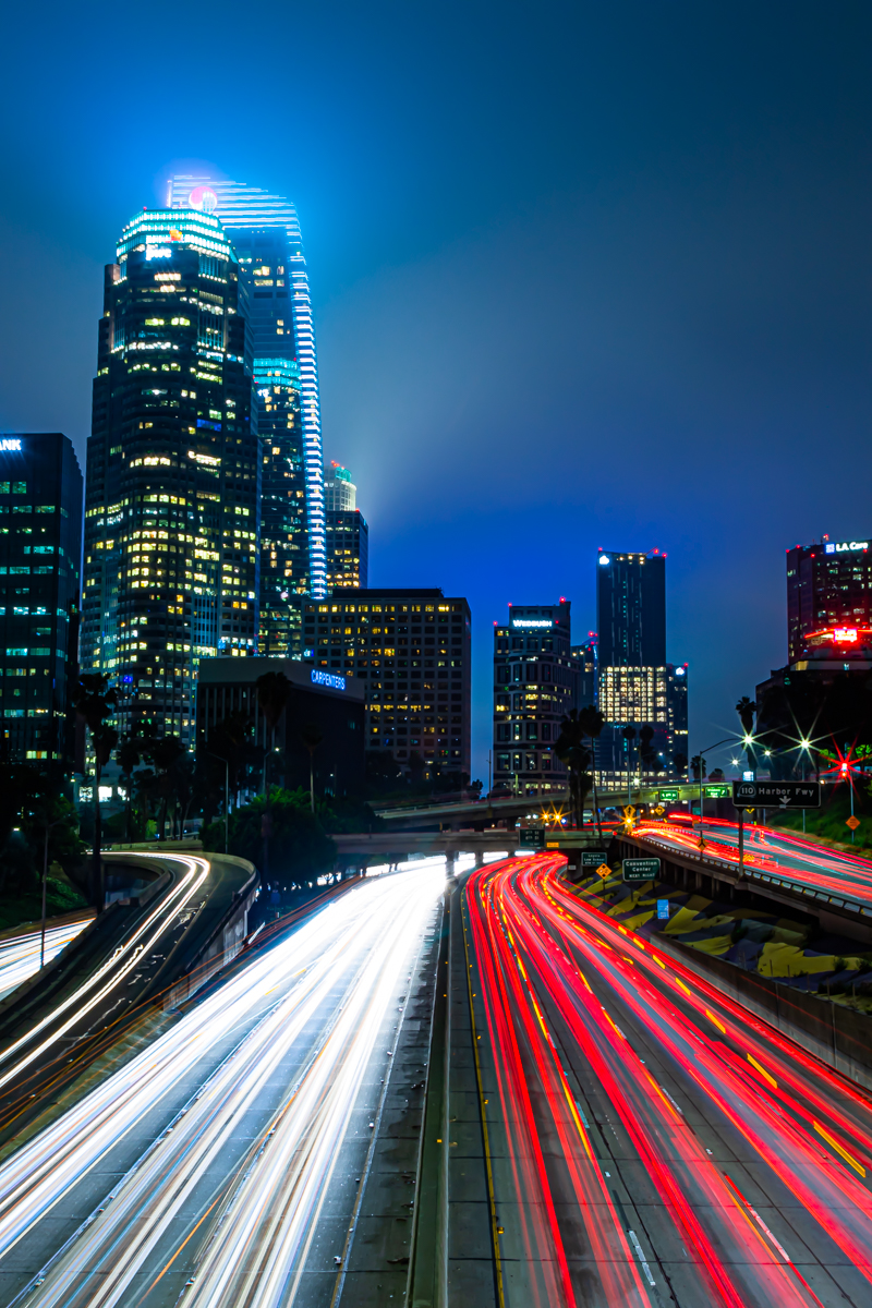 Downtown Los Angeles at night — red and white light streaks converge on the freeway